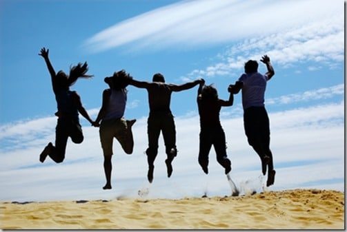 group of friends jumps on sand, rear view